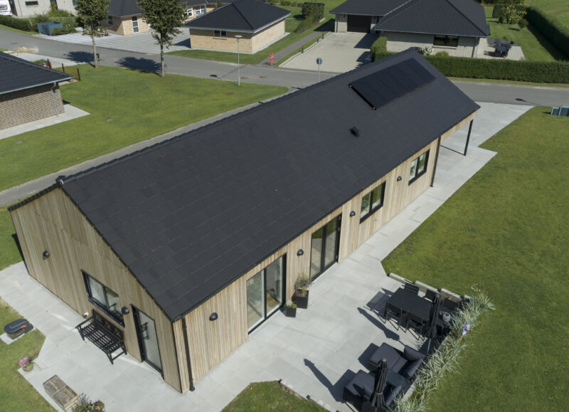 Vi Bygger Vejle: Dronefoto af moderne træhus med sort tag, solceller og stor terrasse i villakvarter.