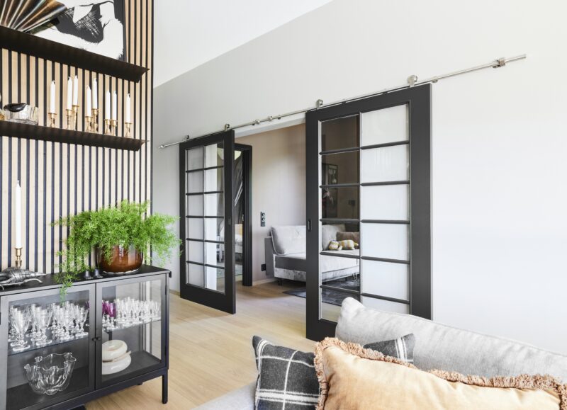 Vi Bygger Vejle: Moderne stue med skydedøre, grøn plante, lys trægulv og grå sofa.