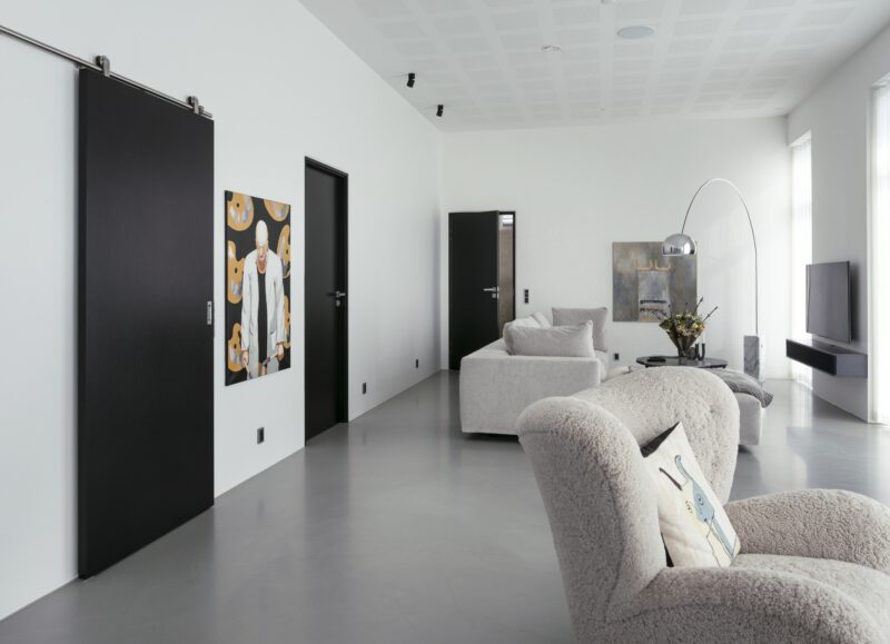 Vi Bygger Vejle: Minimalistisk stue med hvide vægge, mørke døre, gråt gulv og unikt loft.
