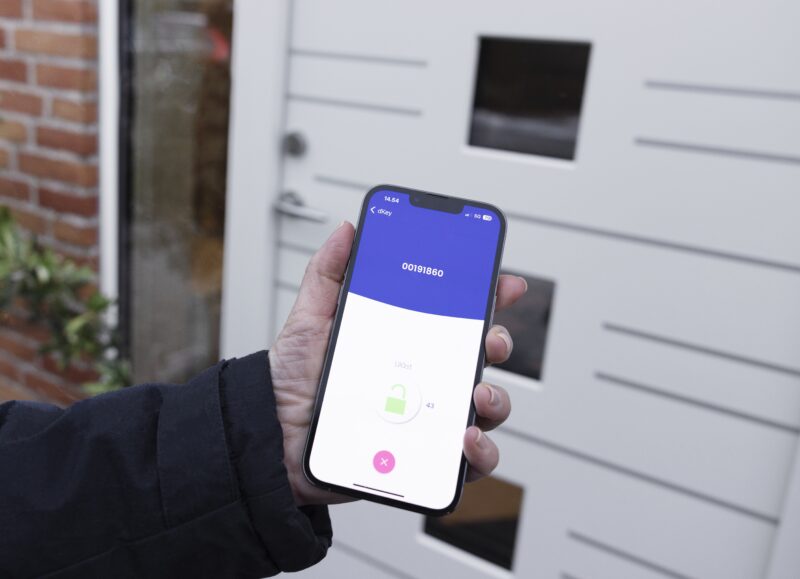 Vi Bygger Vejle: Hånd bruger smartphone med dKey app til at låse op, vist med et grønt hængelås-ikon, foran en dør.