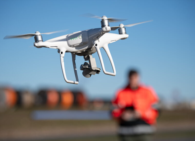 Vi Bygger Vejle: Hvid drone svæver mod blå himmel med en person i orange jakke betjenende i baggrunden.