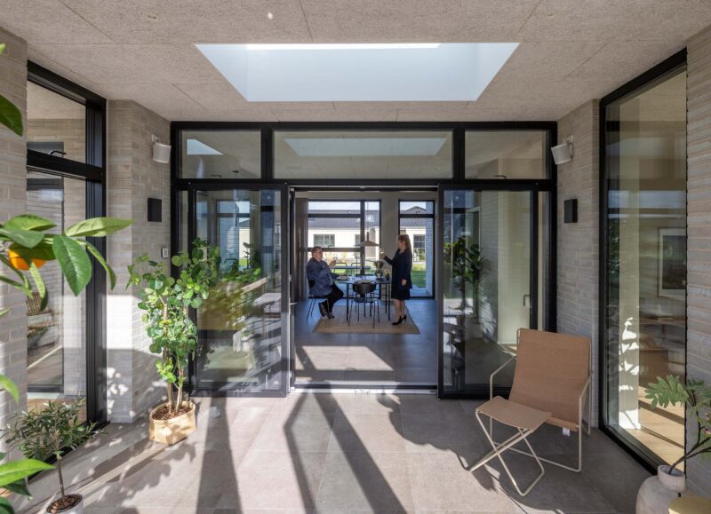 Vi Bygger Vejle: Lyst, moderne hus med glaspartier, indbydende terrasse og to personer indenfor.