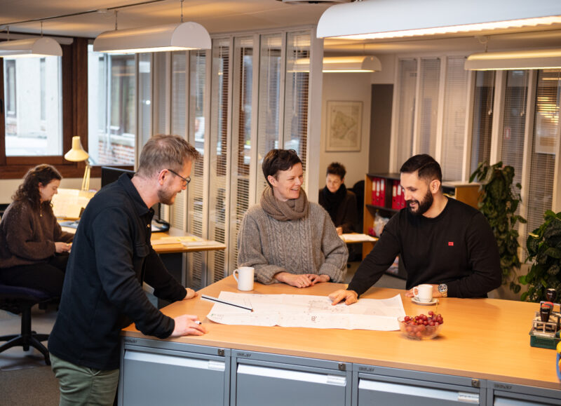 Vi Bygger Vejle: Tre kolleger i dialog om tegninger ved et bord på kontoret.