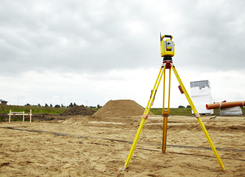 Vi Bygger Vejle: Landmålerudstyr på en byggeplads med sandbunker og materialer under en overskyet himmel.