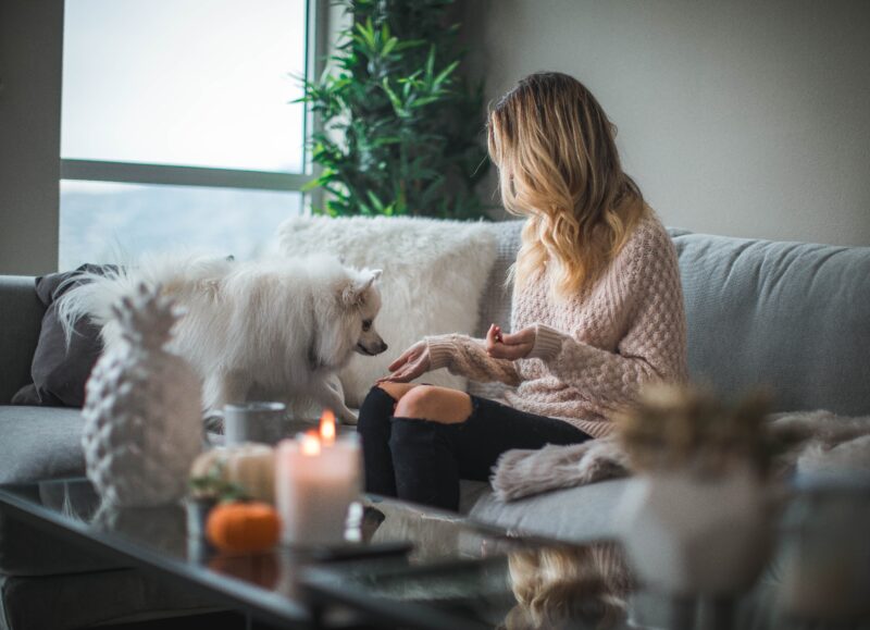 Vi Bygger Vejle: Kvinde på sofa med hvid hund i lyst, hyggeligt hjem med stearinlys.