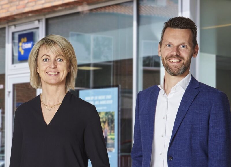 Vi Bygger Vejle: Smilende kvinde og mand i professionelt tøj foran en bygning.