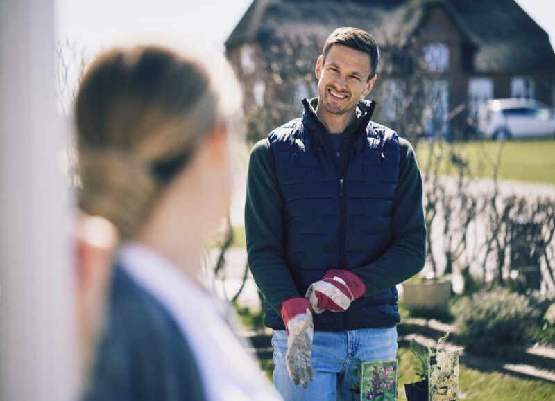 Vi Bygger Vejle: Smilende mand med havehandsker arbejder i haven på en solrig dag.