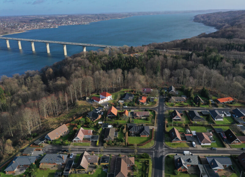 Vi Bygger Vejle: Luftfoto af Vejle Fjordbroen over fjorden, omgivet af skov og et villakvarter.