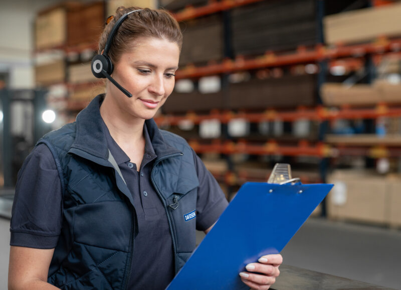 Vi Bygger Vejle: Kvinde med headset og Davidsen-vest tjekker liste på clipboard i et lager.