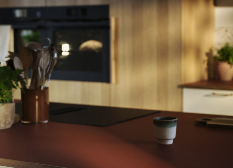 Vi Bygger Vejle: Moderne køkken med terracotta-farvet bordplade, træskabe, ovn og redskaber. Varmt lysindfald.