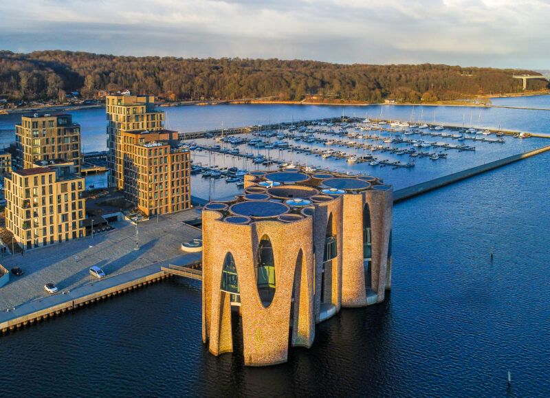 Vi Bygger Vejle: Det ikoniske byggeri Bølgen ved Vejle Fjord, omgivet af moderne boliger og marina.
