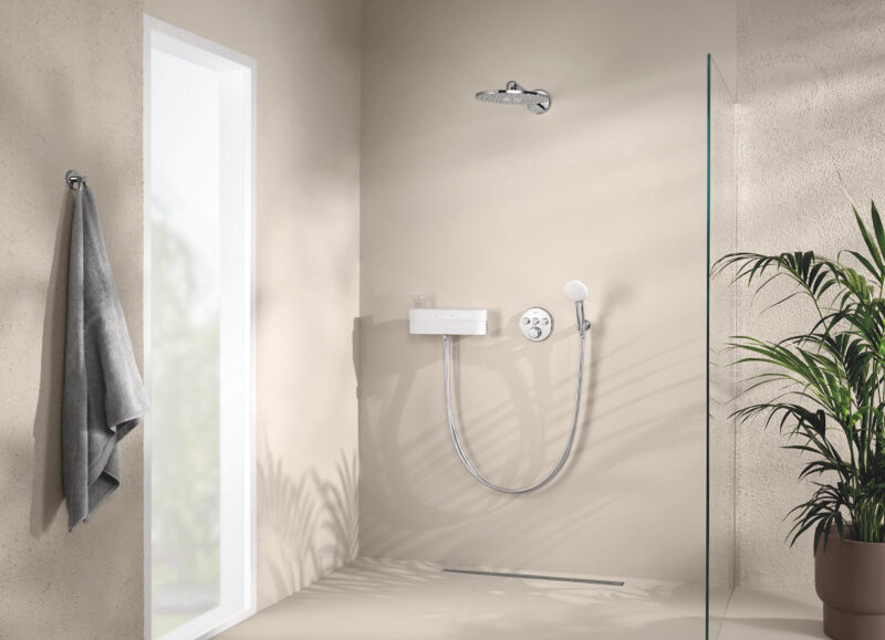 Vi Bygger Vejle: Minimalistisk bruseniche i beige nuancer med loft- og håndbruser, glasvæg, lineært afløb og potteplante.