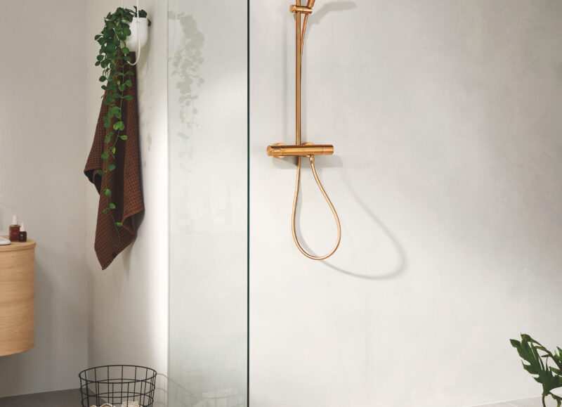 Vi Bygger Vejle: Moderne badeværelse med bruseniche i glas og rosaguld armatur. Hængende plante og håndklæde.