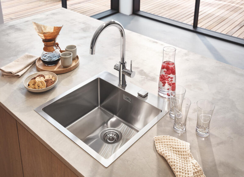 Vi Bygger Vejle: Moderne køkkenbord med stålvask, kromarmatur, kaffebrygger, småkager og kande med hindbærvand.
