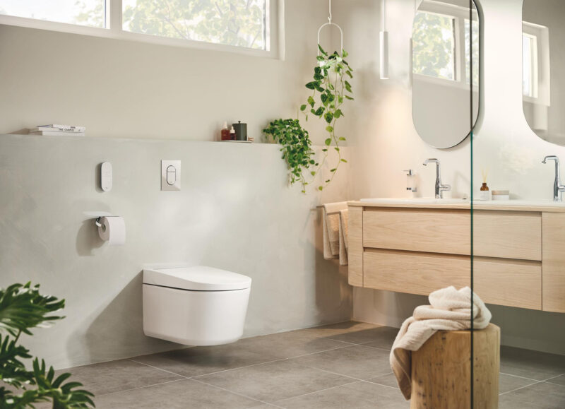 Vi Bygger Vejle: Moderne badeværelse med væghængt toilet, vaskeskab i træ, to spejle og planter.