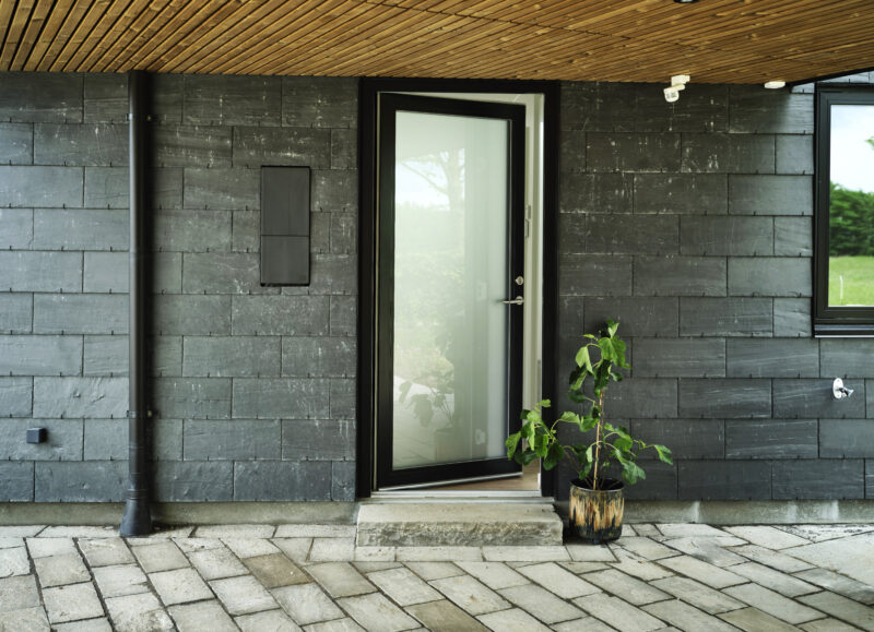 Vi Bygger Vejle: Moderne indgang med skifertfliser, træloft, åben glasdør og potteplante.