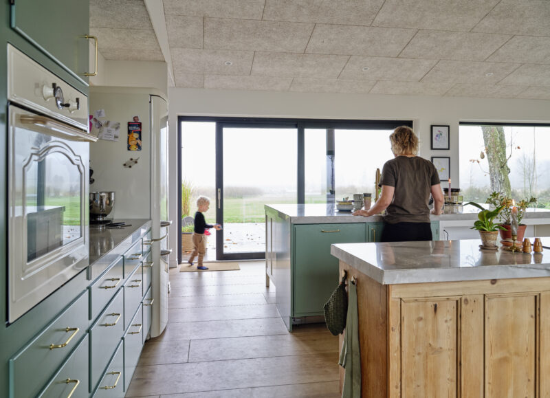 Vi Bygger Vejle: Familie i lyst, moderne køkken med grønne skabe, lydregulerende loft og udsigt til naturen.
