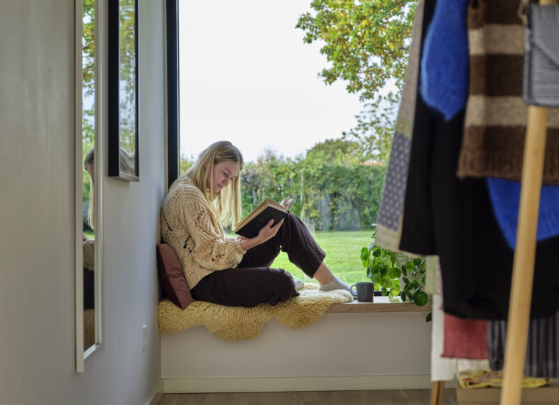 Vi Bygger Vejle: En ung kvinde læser en bog i en vindueskarm med udsigt til grøn have.