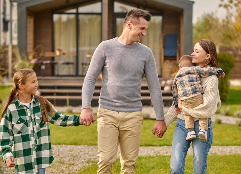 Vi Bygger Vejle: Lykkelig familie går hånd i hånd. Mor bærer baby, far holder datterens hånd foran et nyt hus.