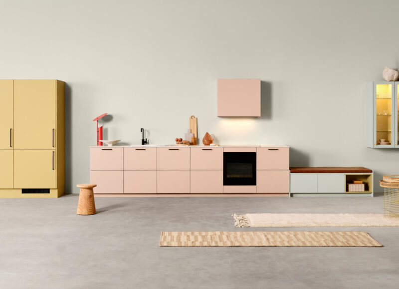 Vi Bygger Vejle: Lyst, moderne køkken/alrum med gule og rosa skabe, blå vitriner og minimalistisk indretning.