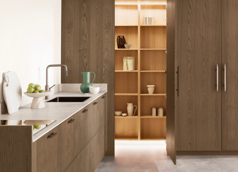 Vi Bygger Vejle: Moderne køkken med mørke træskabe, lys bordplade og åbent spisekammer med lyse træhylder.