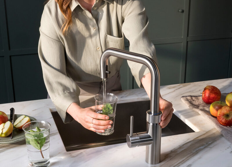 Vi Bygger Vejle: Kvinde fylder et glas med vand og mynte fra køkkenarmatur på en marmorbordplade.